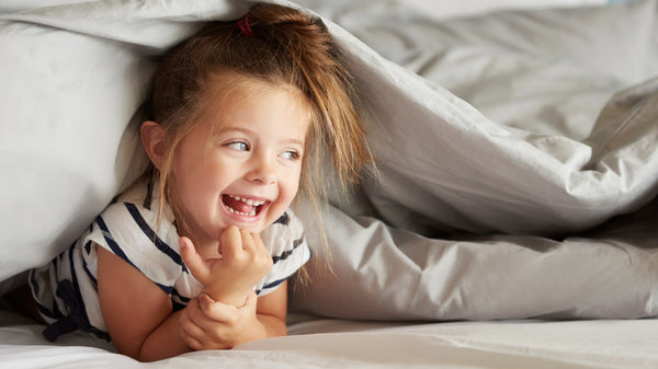 Vidám lány gyerek fekszik az ágynemű alatt